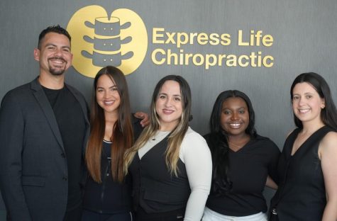 Team of five professionals posing in front of a gold Express Life Chiropractic sign, smiling at the camera.