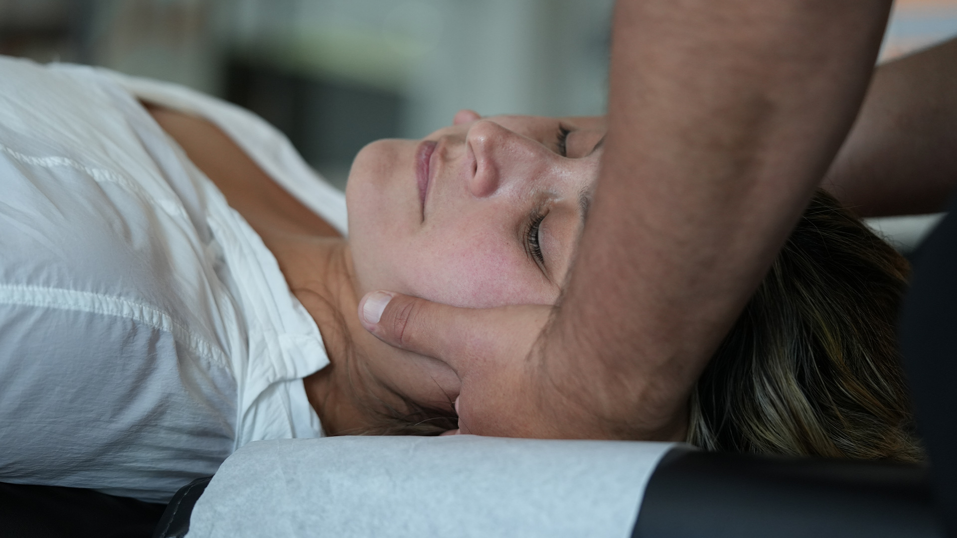 Person lying on a massage table with another person supporting their neck and head during a treatment