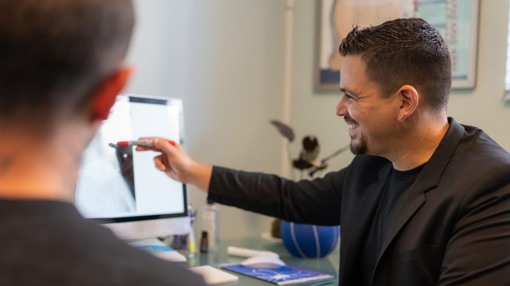 Chiropractic adjustment after a flight - Express Life Chiropractic | Chiropractor Fort Lauderdale. Two professionals in a clinic review an X-ray on a computer monitor, with one pointing at the screen as the other observes.