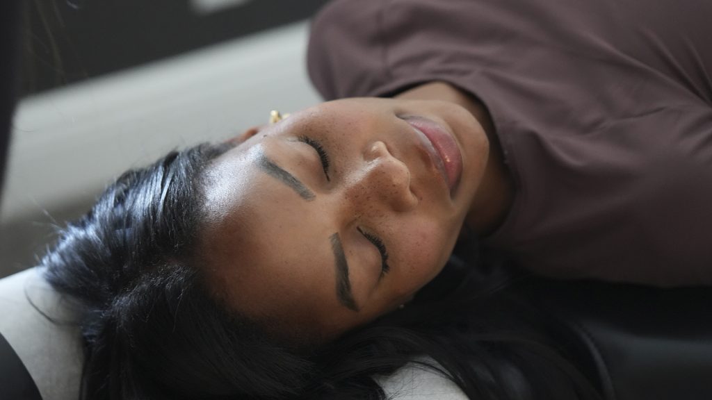 What Should You Wear to a Chiropractic Appointment - Express Life Chiropractic | Chiropractor Fort Lauderdale. Woman with dark hair lying down on her back with eyes closed, wearing a maroon top.